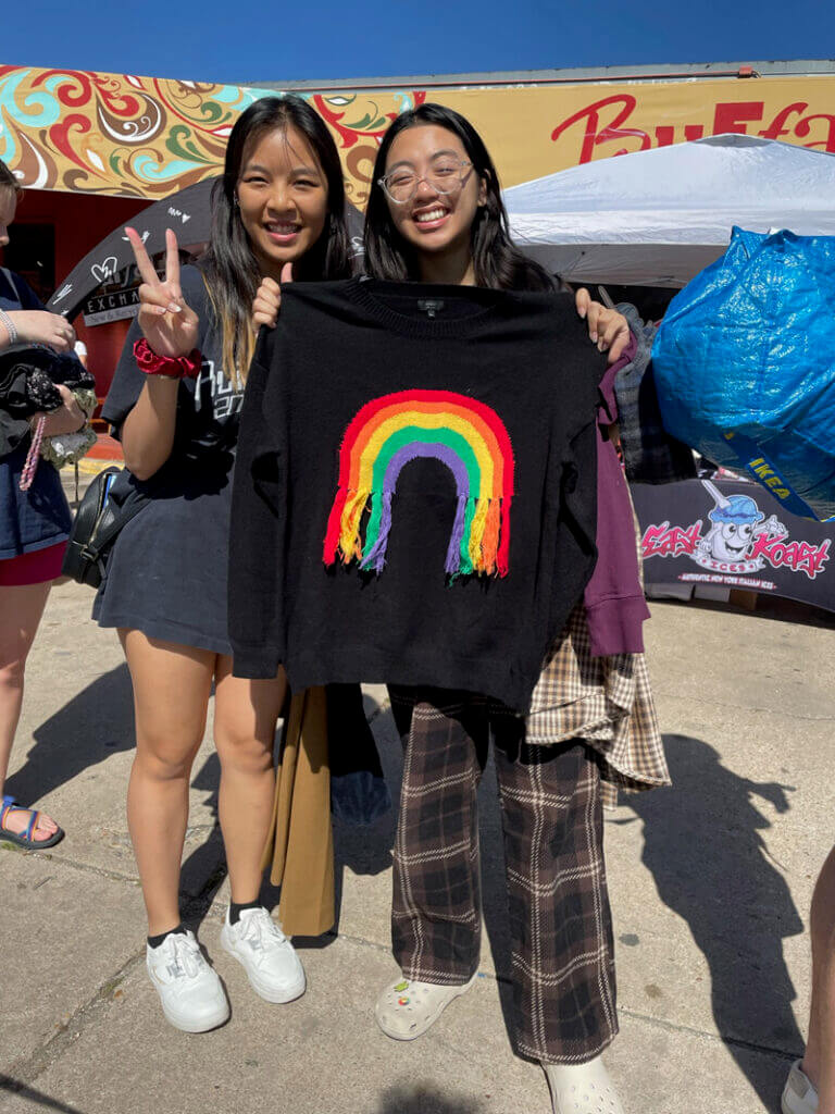 Two shoppers in front of Buffalo Exchange holding up a rainbow sweater they bought at the Earth Day $1 Sale