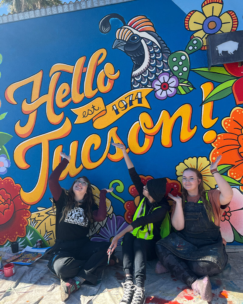 emma, katie, and quinn sitting underneath the mural