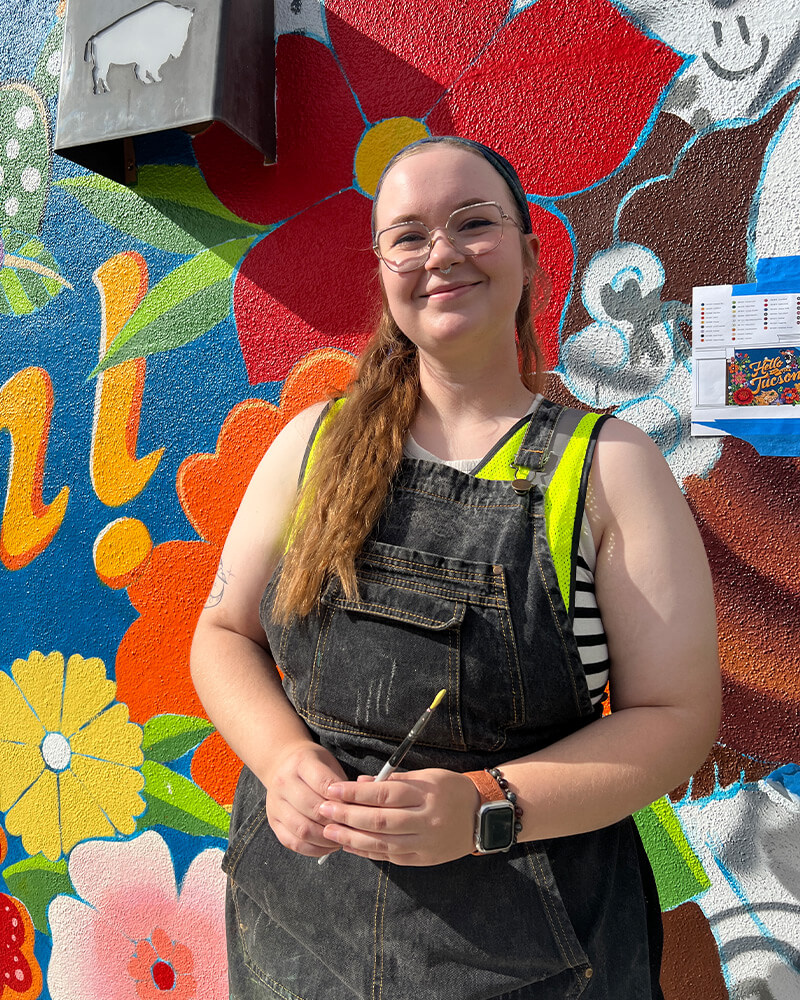 quinn posing in front of the mural holding a paintbrush