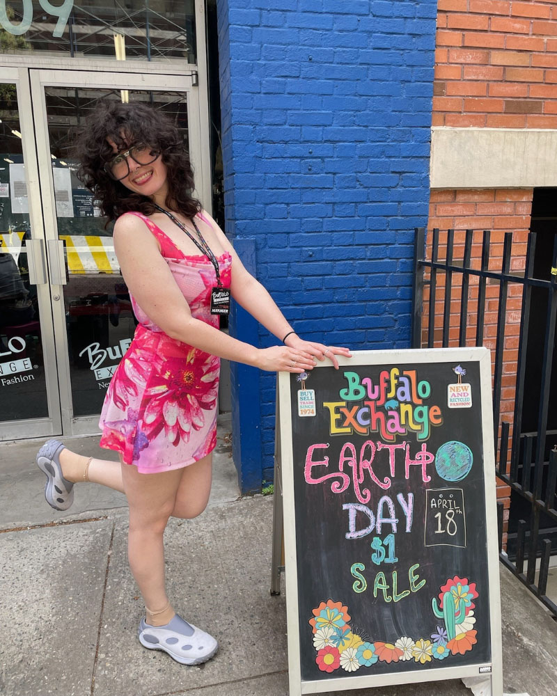 Buffalo Exchange employee posing with a sandwich board promoting the Earth Day $1 Sale